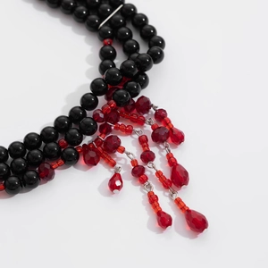 Close-up of black beads and red crystal tassels with a water drop pendant on the necklace