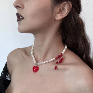 Detail of layered pearl choker featuring a red heart pendant and crystal fringe on model
