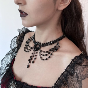 Detail van gotische zwarte kralenketting met lagen strik en kwastje om de hals van model
