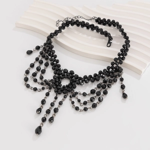 Gothic meerlagige zwarte kralenketting met kruishanger en kralenkwastjes op wit decor