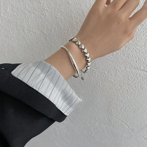 Nahaufnahme eines silbernen Herzketten-Armbands und glatten Armreif-Sets am Handgelenk