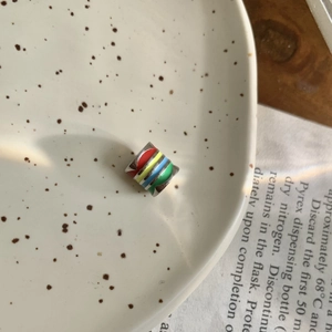 Detail of a cylindrical rainbow enamel bead with colorful stripes on a ceramic plate