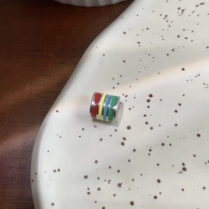 Macro detail of a colorful enamel cylinder bead with multi-color stripes on a ceramic plate