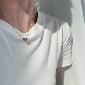 Detailed shot of rainbow enamel cylinder pendant on silver chain worn on a white T-shirt