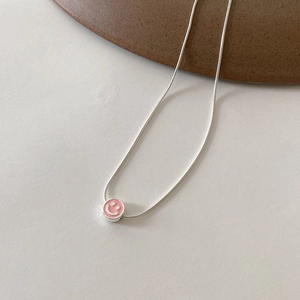 Gros plan d'un pendentif sourire en émail rose sur une chaîne serpent argentée