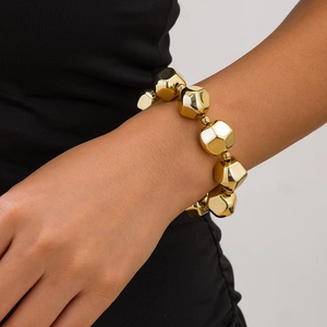 Vista detallada de pulsera dorada con cuentas geométricas irregulares en la muñeca