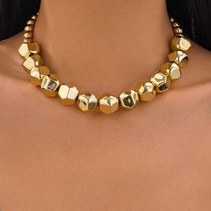 Detalle de un collar de grandes cuentas geométricas doradas lucido por una modelo