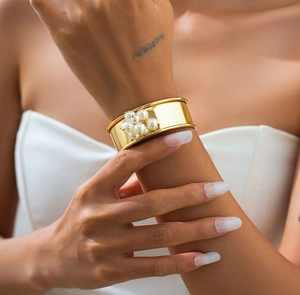Dettaglio di un bracciale rigido dorato aperto con un grappolo di sei perle bianche