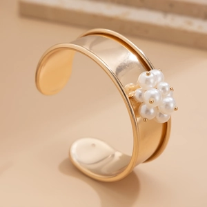 Dettaglio ravvicinato di un ampio bracciale aperto dorato con elegante ciondolo di perle