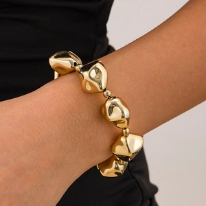 Detalle de pulsera dorada con cuentas irregulares y un acabado metálico pulido brillante