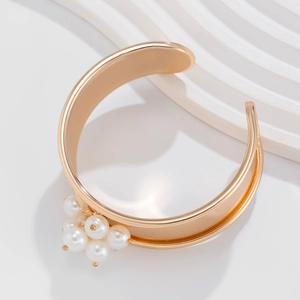 Dettaglio di un bracciale aperto dorato con un elegante grappolo di perle bianche