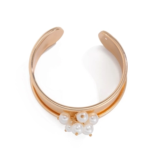 Dettaglio ravvicinato di un bracciale rigido dorato aperto con eleganti perle bianche