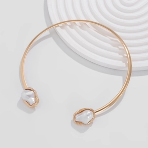 Détail d'un collier choker ouvert en métal doré orné de deux perles baroques