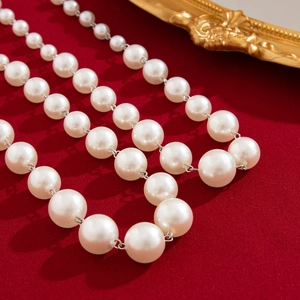 Close-up of elegant faux pearl necklace with metallic clasp on luxury red fabric background