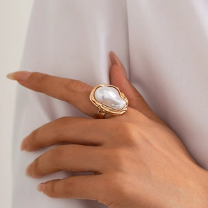 Gros plan d'une bague dorée ornée d'une perle baroque sur tissu blanc plissé