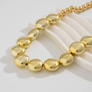 Detalle de un collar de bolas doradas con perlas pulidas sobre un soporte blanco