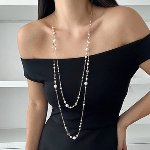 Detail view of double-layer gold pearl necklace with floral charms on black dress