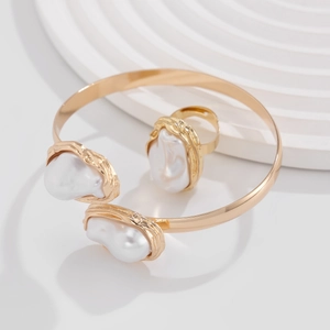 Ensemble bracelet et bague minimaliste en métal doré avec perles baroques sur socle blanc