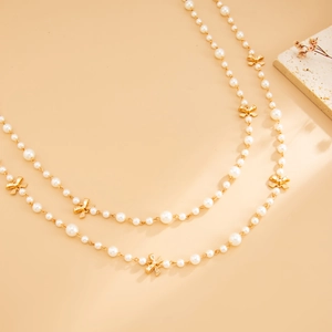 Close-up of double-layer faux pearl necklace featuring gold bow pendants and elegant chain