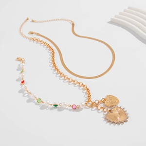 Detail einer mehrlagigen Goldkette mit Herz- und Sonnenanhänger sowie Perlenakzenten