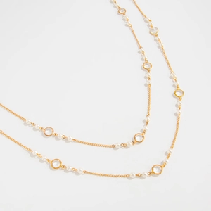 Detail of long gold station necklace with white pearls and round clear crystals
