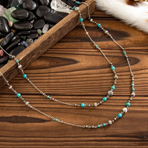 Detail of silver long necklace featuring turquoise beads and wavy metallic accents