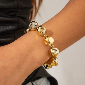 Detalle de una pulsera dorada de cuentas irregulares gruesas en la muñeca mujer