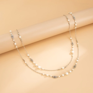 Close-up of elegant pearl and silver flower charms on a long chain sweater necklace