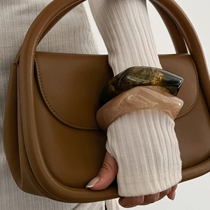Close-up of brown leather handbag and acrylic resin bracelets on model in white knitwear
