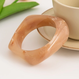 Detail of a wide acrylic bangle featuring a brown and white marble pattern texture