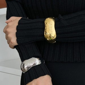 Detailed view of wide metallic cuffs with hammer texture in gold and silver finishes