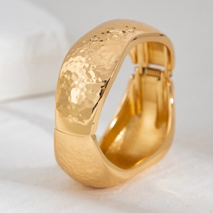 Close-up of golden wide bangle with liquid metal hammered texture and spring hinge