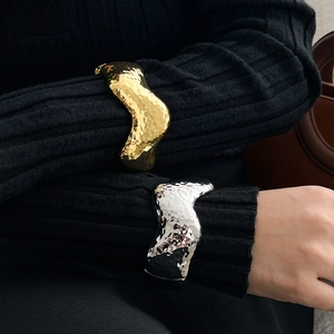 Detail view of wavy metallic bangles with hammered texture worn over a black sweater sleeve