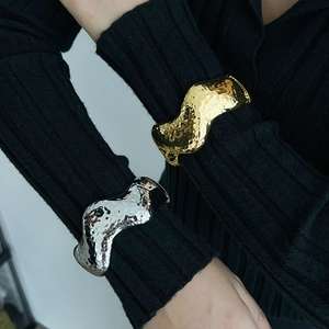 Detail of liquid metal texture bracelets in gold and silver finish with wavy ripples