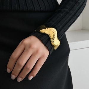 Close-up of golden wide cuff bracelet with wavy edges and hammered texture on wrist