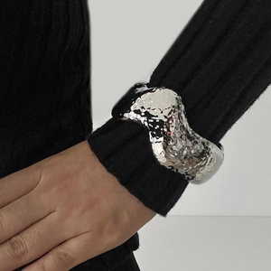 Detailed macro view of silver liquid metal wide cuff bracelet with wavy textured edges