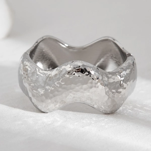 Macro detail of silver liquid metal bracelet featuring a textured hammered finish and wavy edges