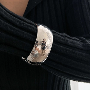 Detail of silver hammered liquid metal wide bracelet on model with dark background