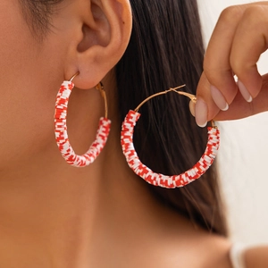Close-up of red and white polymer clay hoop earrings with golden clasp detail