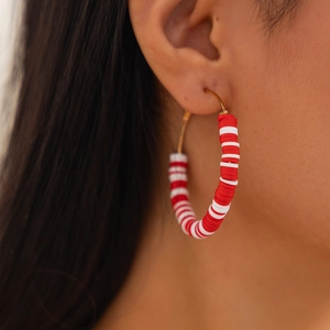 Macro side view of a gold hoop earring with red and white clay beads worn by a woman