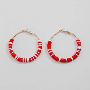 Detailed view of large gold hoop earrings with red and white festive clay beads
