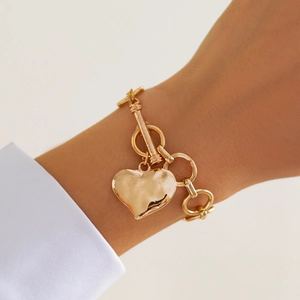 Vista macro del bracciale dorato con pendente a cuore, catena a maglie e chiusura a T