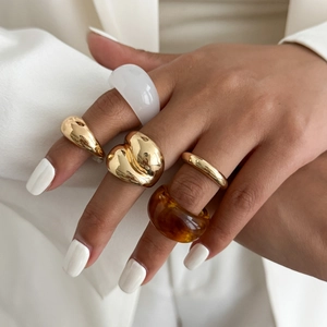 Close-up van gouden metalen ringenset met amberkleurige hars en witte acrylringen