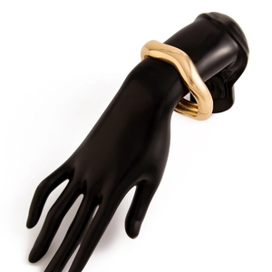 Detailed view of the wavy golden metal wide bracelet with a glossy finish and hinge clasp