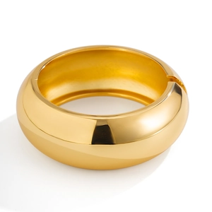 Macro shot of wide gold metallic bracelet featuring smooth mirror polish and spring hinge