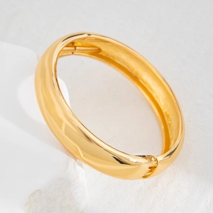 Close-up of gold metal spring cuff bracelet showing the hinge mechanism on a white stone
