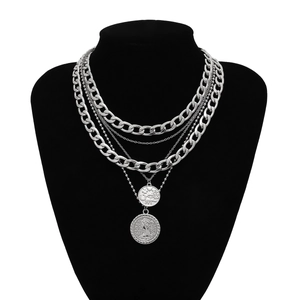 Detail of layered silver necklaces with coins on a black bust against white background