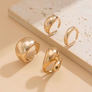 Vue détaillée de quatre bagues goutte dorées minimalistes sur un socle en pierre beige