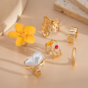 Detail of six varied rings with baroque pearl, yellow flower enamel, and colorful gems