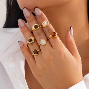 Detail of 6-piece gold-tone ring set with faux gemstones worn by model on white background